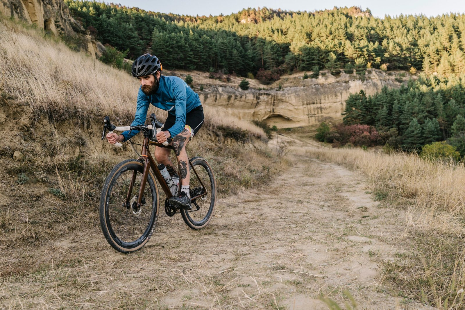 Gravel Pantelleria 2026 uomo in bicicletta su sterrato con ruote sporche di terra, casco e barba, pedalando tra sentieri e paesaggi mediterranei.